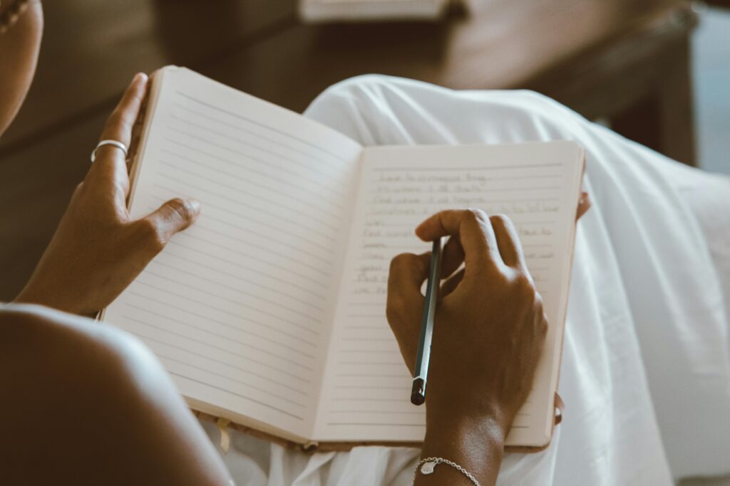 Close-up of hands writing in a journal with a pencil on a seated lap.