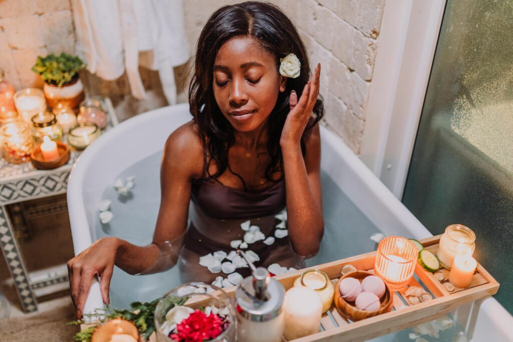 Peaceful spa scene with African American woman in bathtub, surrounded by candles and petals.