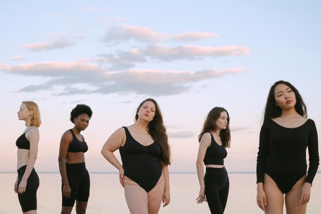 Five diverse women in swimwear posing confidently outdoors, celebrating body positivity and sisterhood.